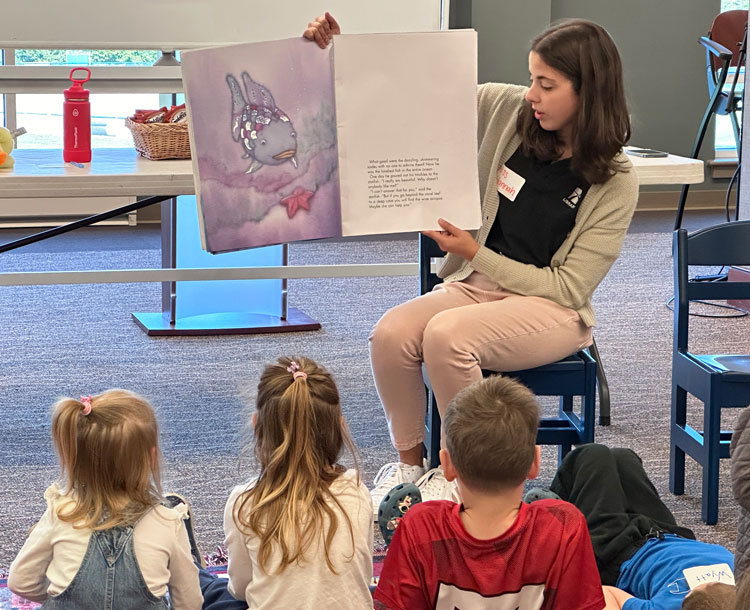 student teacher reading and showing a book to young kids